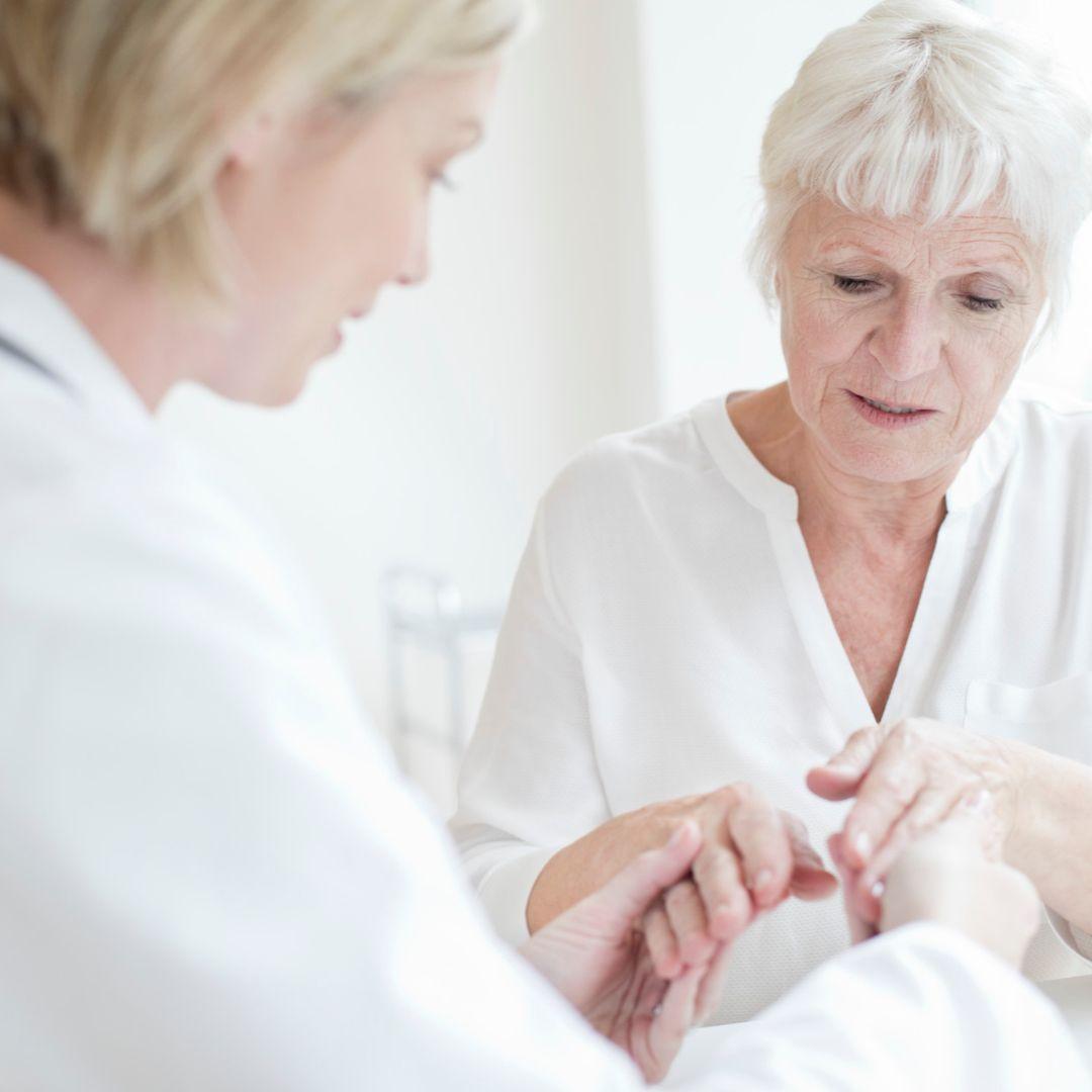 A hand therapist with dark hair and glasses examines the hand of a woman with arthritis
