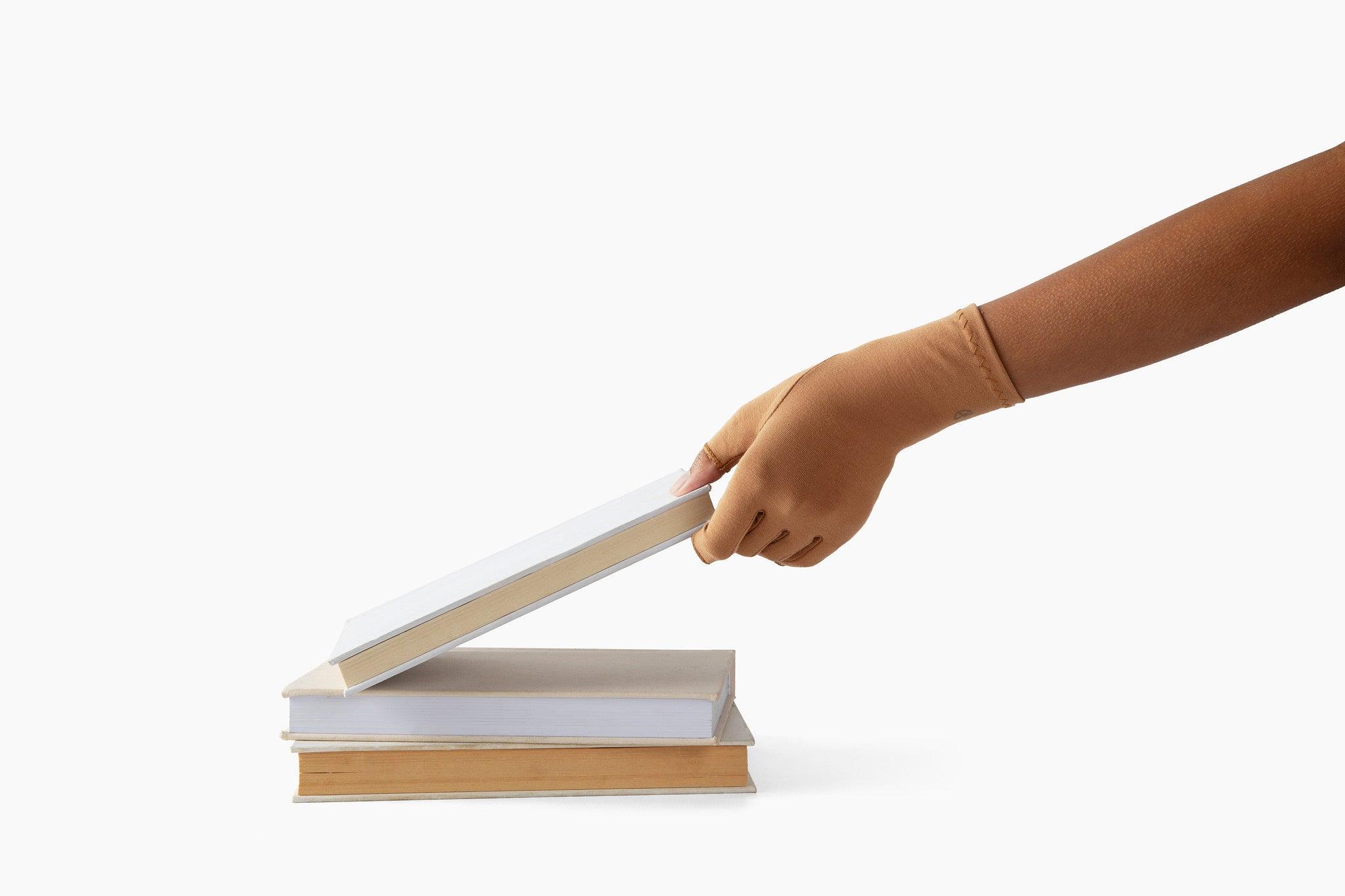 Cinnamon Brown Compression Gloves on a woman's hand picking up a book