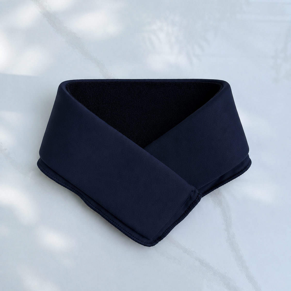 A midnight blue cooling neck wrap laid flat on a light gray marble-textured background.