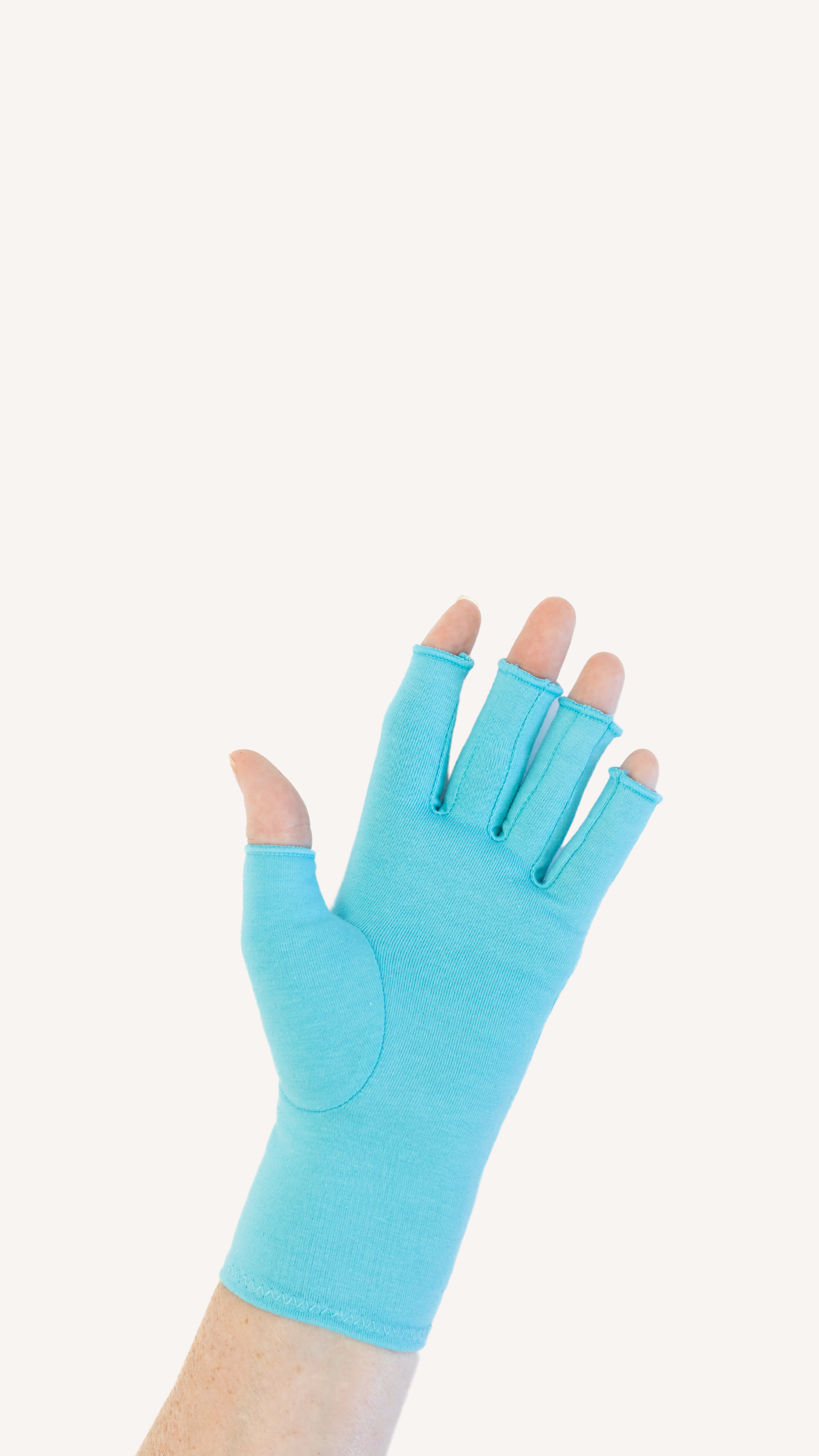 Close up of the hand of a woman with arthritis wearing Aqua Blue Compression Gloves on a beige background.