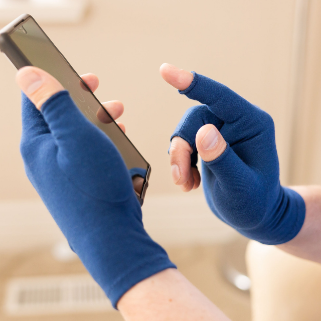 A close-up of hands of a woman with arthritis, wearing Marine Blue Compression Gloves and texting on her phone
