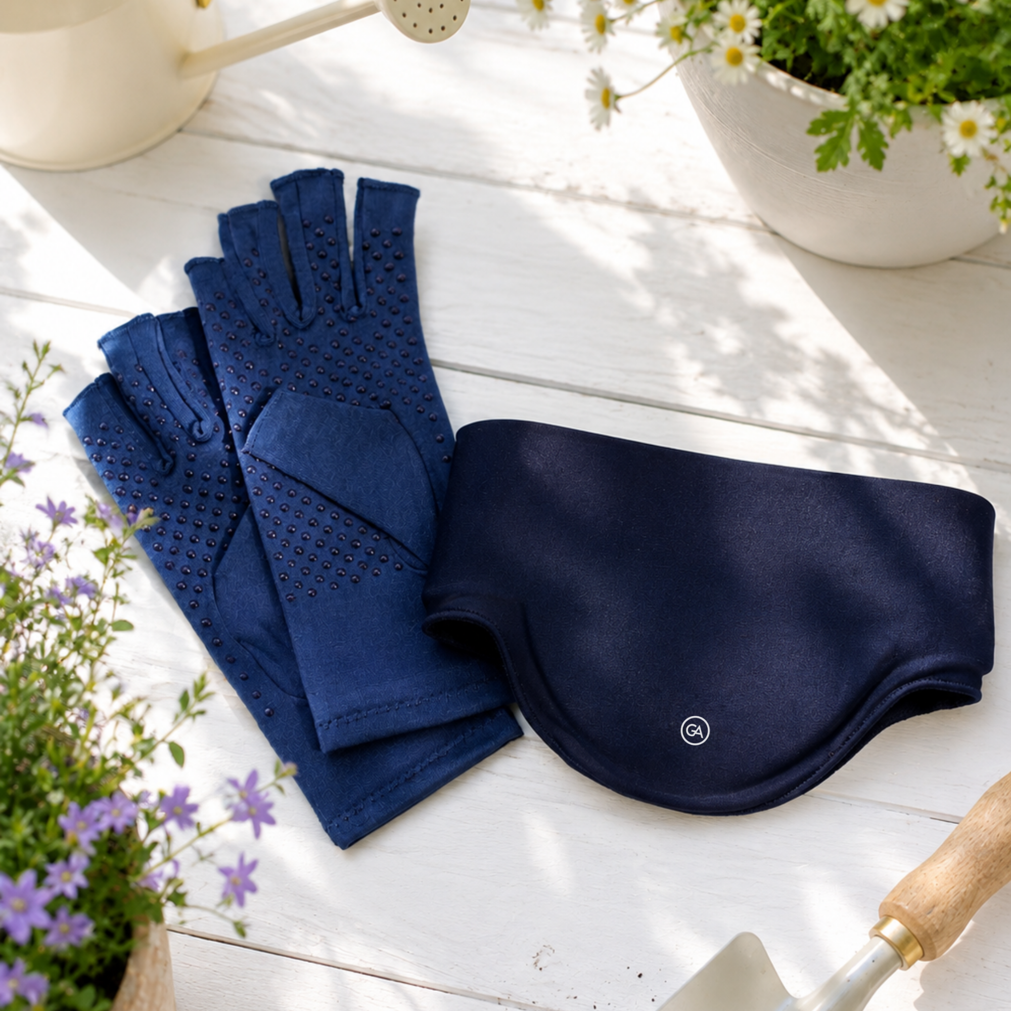 A pair of Marine Blue Extra Grip Compression Gloves with silicone dots and a matching Midnight Blue Cooling Neck Wrap, arranged on a white wooden surface with gardening props like a watering can, potted flowers, and a trowel.