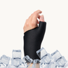 A close-up of a hand and wrist wearing a jet black cooling compression sleeve for thumb and wrist, with ice cubes around it on a plain light background.