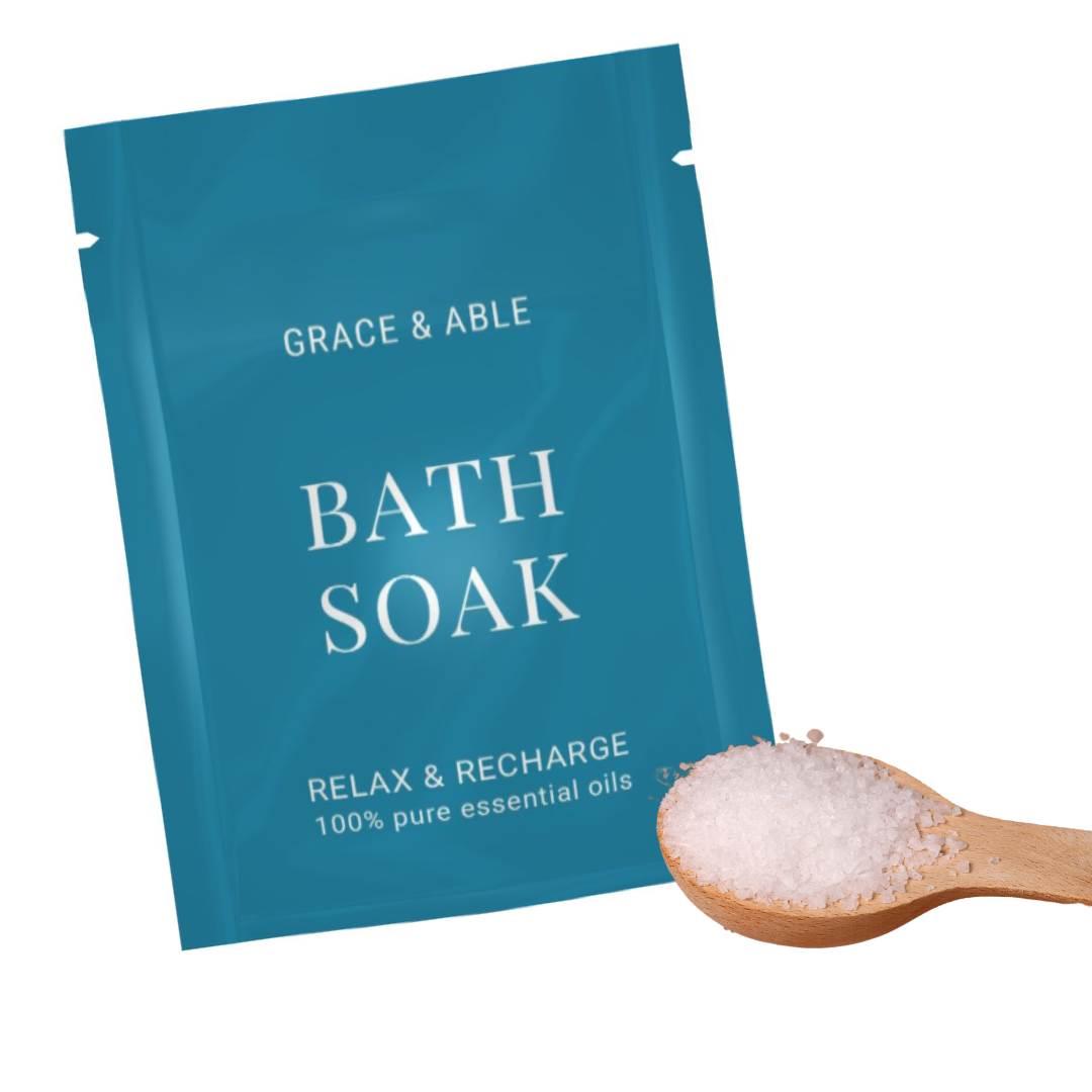 A teal bag that says 'Grace & Able Bath Soak Relax & Recharge 100% Pure Essential Oils' next to a wooden spoon full of bath salt that is helpful for arthritis
