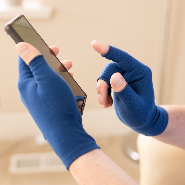 A close-up of hands of a woman with arthritis, wearing Marine Blue Compression Gloves and texting on her phone