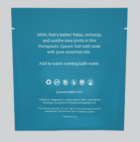 Close-up of the back of a teal-colored Grace & Able Bath Soak package featuring white lettering. The text reads: 'Ahhh, that's better! Relax, recharge, and soothe sore joints in this therapeutic Epsom Salt bath soak with pure essential oils. Add to warm running bath water. /graceandable.com/ Ingredients: Magnesium sulfate (Epsom salt), Lemongrass, Rosemary, Eucalyptus & Peppermint Essential Oils.'
