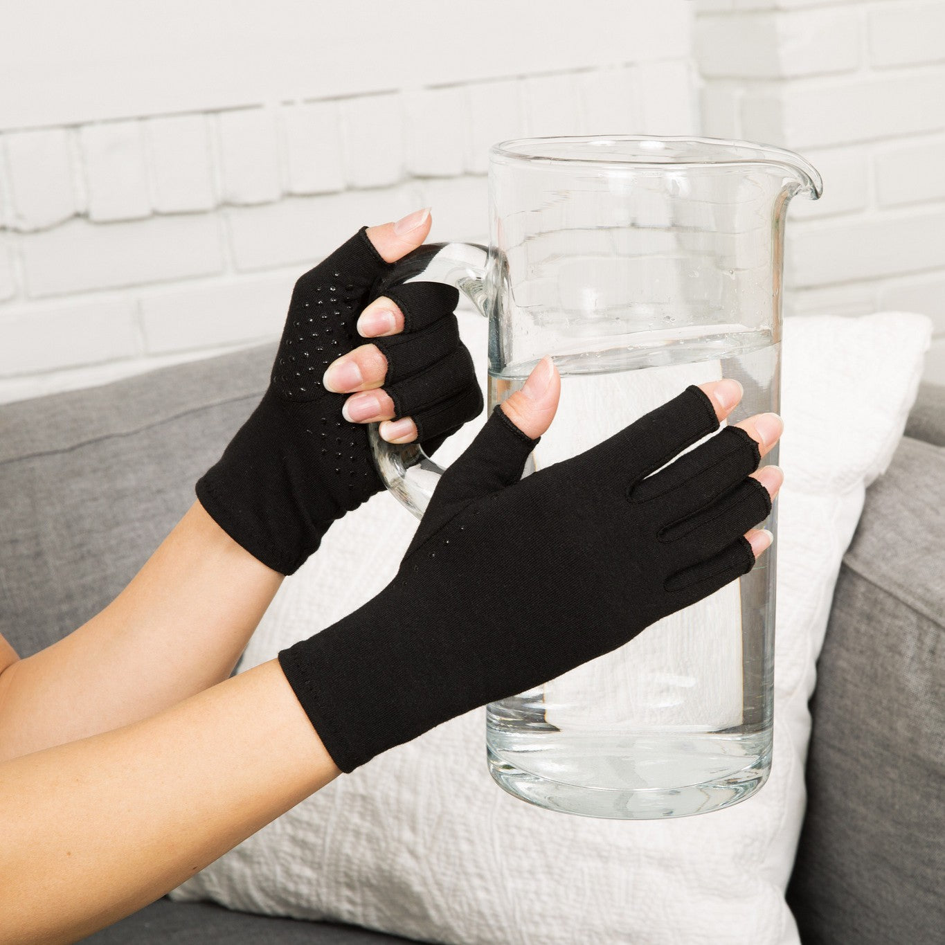 classic black compression gloves with silicone dots on palm worn by a pair of hands with arthritis holding a pitcher