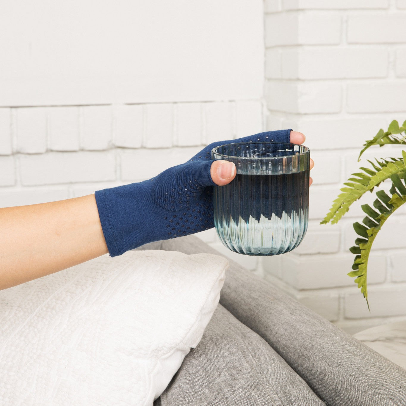 marine blue compression gloves with silicone dots on palm worn by a hand with arthritis holding a glass of water