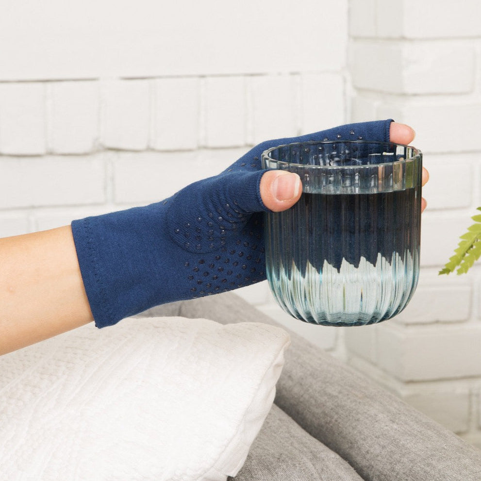 marine blue compression gloves with silicone dots on palm worn by a hand with arthritis holding a glass of water
