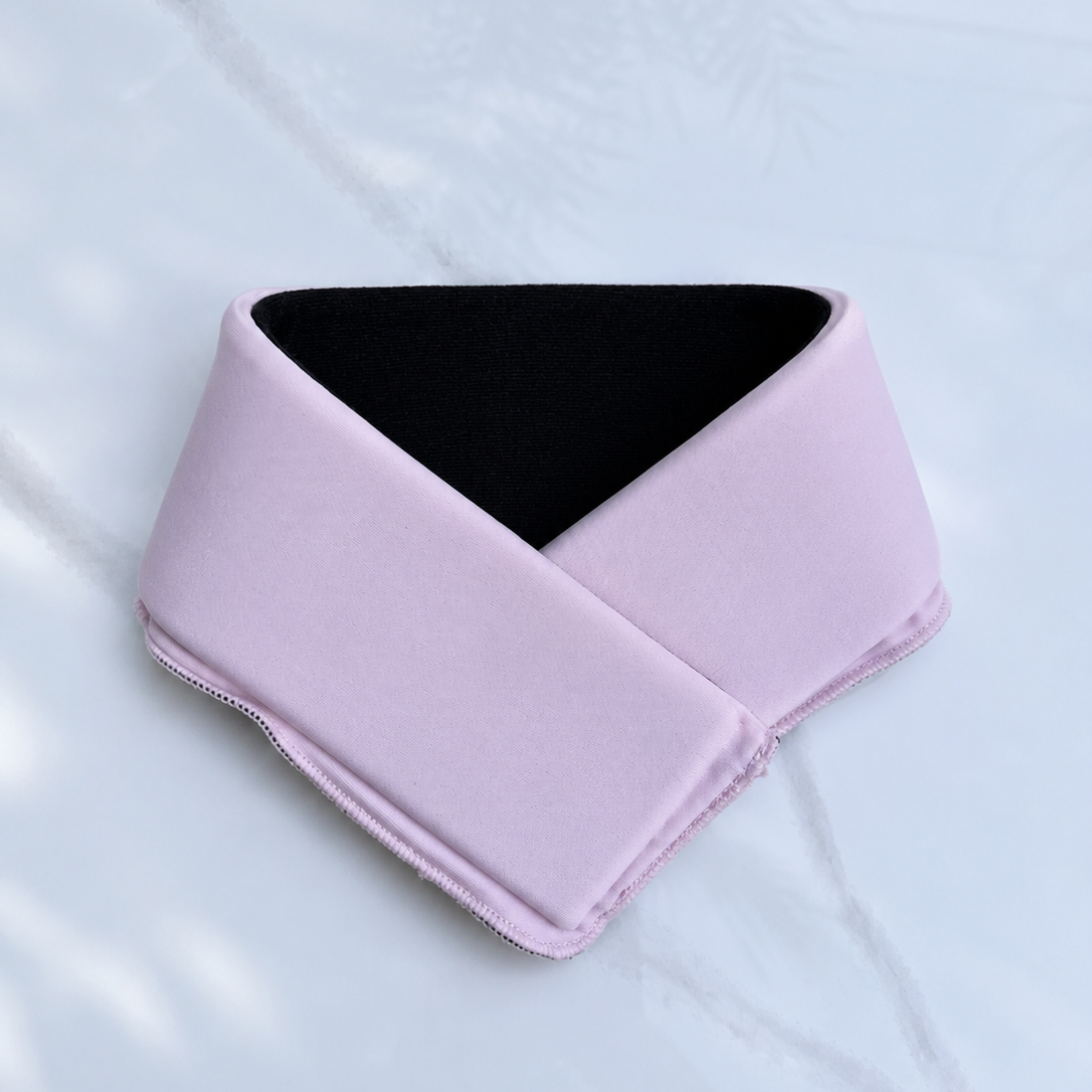 A pastel pink cooling neck wrap laid flat on a light gray marble-textured background.