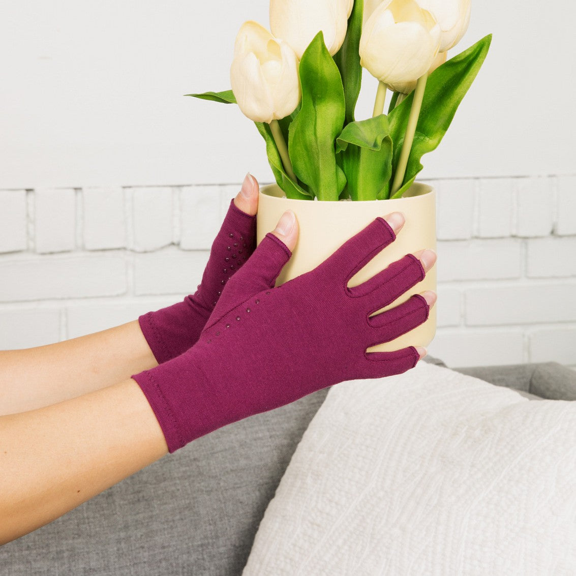 plum purple compression gloves with silicone dots on palm worn by a pair of hands with arthritis holding a flower vase